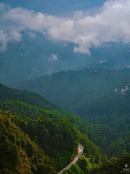 The serpentine roads of the Himalayas. This shot captures the moody, atmospheric conditions of a monsoon drive, with low-hanging clouds blanketing the lush green hills.