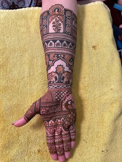This design features a beautiful peacock on the palm, with its feathers forming an intricate pattern. The arm has bands of elephants and architectural details.