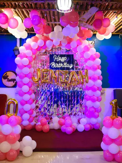 The birthday party decoration setup, featuring a pink and white balloon arch and a "Happy Birthday Jeniah" sign.
