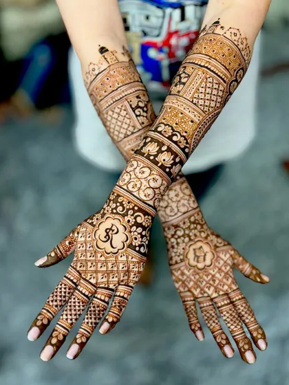 This design features the Om symbol and the bride's initial "R" on the palms, surrounded by intricate jaali and floral patterns.