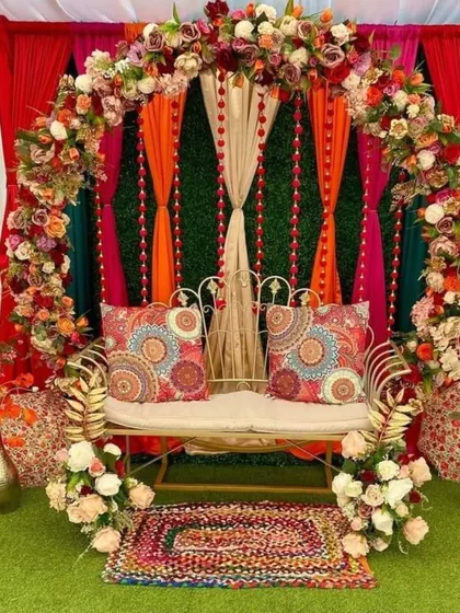 A beautiful Mehndi seating arrangement with a colorful backdrop of drapes and a leafy green wall. The traditional printed cushions and floral details complete this vibrant and folksy look.