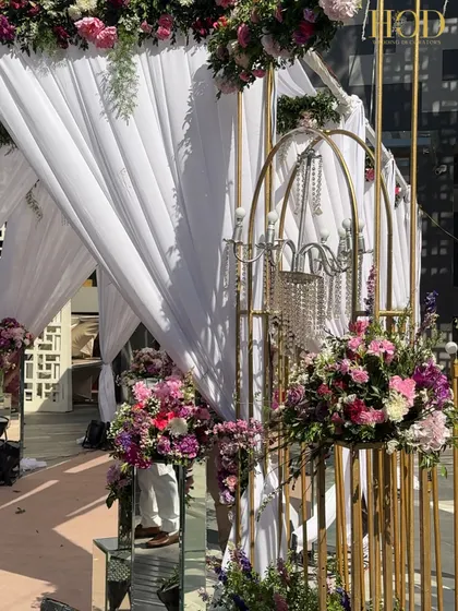 This elegant white draped entrance is accented with gold-caged chandeliers and lush pink floral arrangements. The mirrored pedestals add a touch of modern glamour to the soft, romantic setup.
