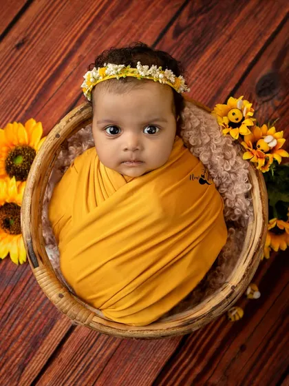 An adorable sitter session portrait of a baby wrapped in yellow, looking curiously at the camera.