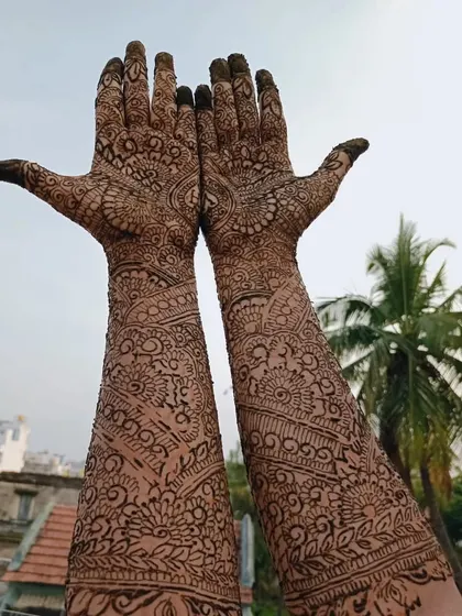 The final result of a full bridal mehendi, held up against the sky. The design is packed with intricate details from fingers to elbows.