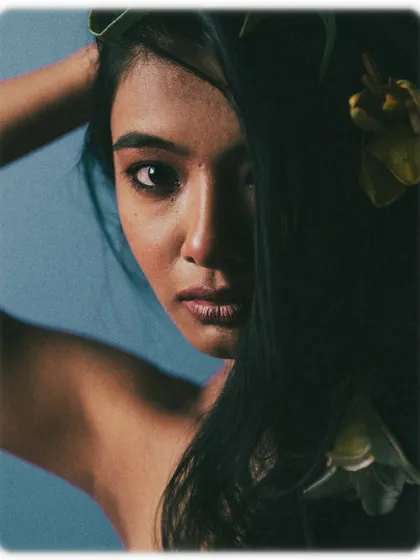 Here, the model's hair is used to create a sense of mystery, covering one side of her face. The direct gaze from her visible eye is powerful and intriguing. The flowers in her hair add a touch of organic beauty to the composition.