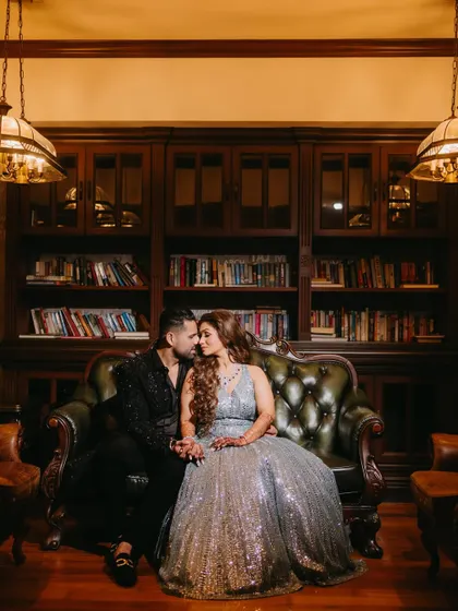 An intimate portrait of a couple on a leather couch, holding hands and sharing a close moment, with warm lighting creating a romantic mood.