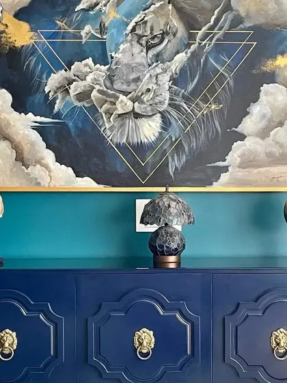 The intense gaze of the lion, captured in this acrylic painting. The artwork is framed and placed above a beautiful navy blue credenza, demonstrating how a custom piece can elevate an interior space.