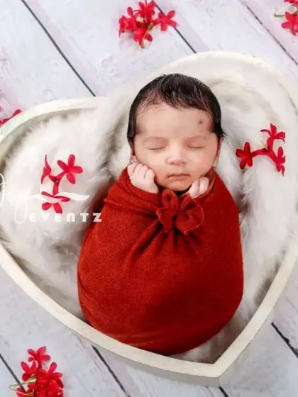 A lovely heart-themed newborn photo. The baby is wrapped in a crimson red swaddle and placed inside a white, heart-shaped bowl, creating a perfect portrait to celebrate your new love.