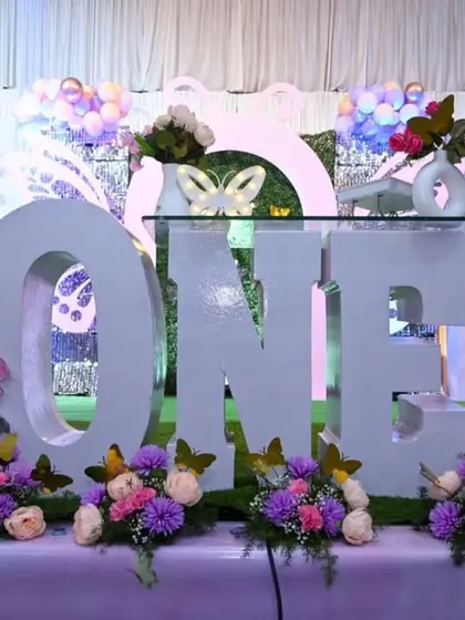 A close-up of the cake table from a butterfly-themed first birthday. The giant 'ONE' prop serves as a fantastic centerpiece, decorated with flowers and butterflies.