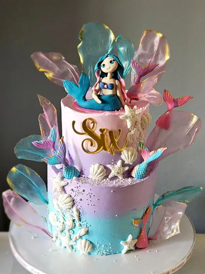 Another angle of the two-tiered mermaid cake, showing the full effect of the pastel ombre buttercream, edible coral, and delicate rice paper sails.