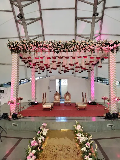 A modern mandap design with chevron-patterned pillars and a ceiling of hanging red flowers.