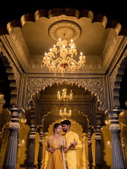A couple stands in a majestic hall with golden lighting and intricate architecture. This shot is perfect for a royal-themed pre-wedding shoot.