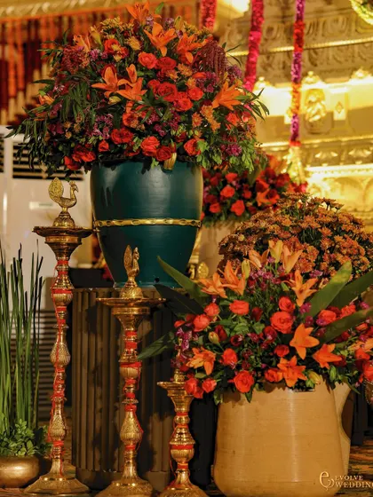 A close-up of the floral arrangements and traditional brass lamps (diyas) used in the Mysore Mandira decor. The combination of vibrant orange and red flowers with polished brass adds a layer of authentic, sacred detail.