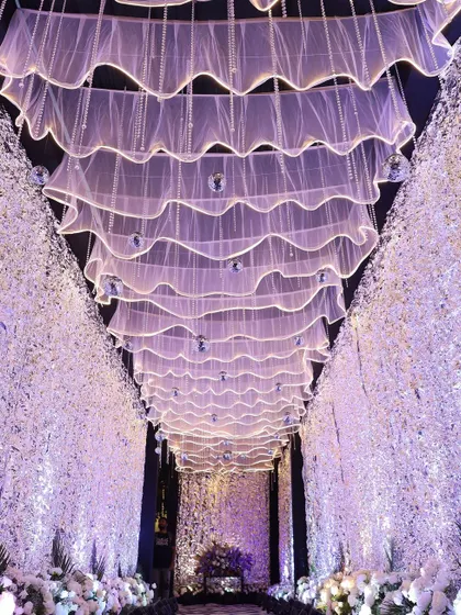 A dreamy sangeet pathway with walls of white flowers and a ceiling of flowing white fabric and mini disco balls.