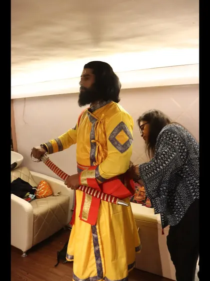 This shot shows the final adjustments being made to the costume and sword. It highlights the attention to detail that goes into creating an authentic historical portrait.