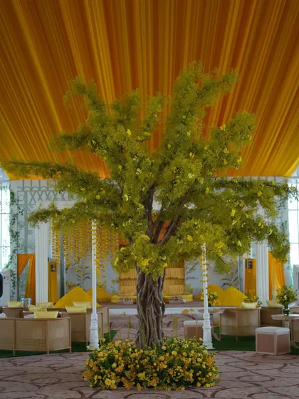 A magnificent 'tree of life' centerpiece with delicate yellow flowers, set against a draped yellow ceiling, created a focal point for the Haldi function.