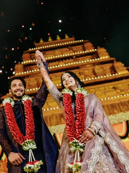 The couple celebrates their union with hands raised in triumph against the backdrop of a beautifully lit temple at night.