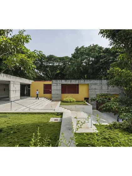 A view of the sports center nestled among the trees. The building's low profile and integration with the ground make it feel like a natural extension of the landscape.