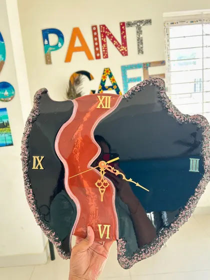 An abstract shaped resin clock in black and orange, held up to show its unique form.