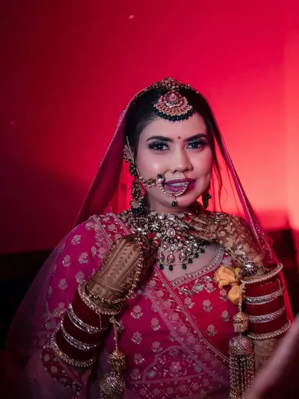 A stunning bridal portrait with dramatic red lighting. The bride looks confidently at the camera, her intricate jewelry and makeup highlighted, creating a bold and beautiful image.