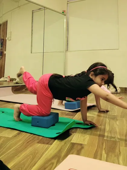 This little yogi uses a block for support in a balancing table top pose, demonstrating how props can help children find stability and proper alignment.