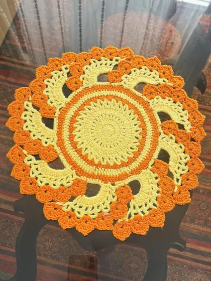 A round crochet thalkosh or table mat in a bright orange and yellow sunburst pattern, laid flat to show the intricate design.