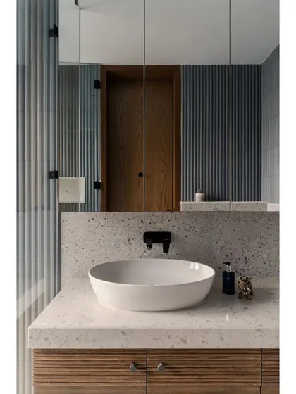 A clean and modern bathroom for the kids' wing at Pràna. The terrazzo countertop and ribbed wood vanity are durable and stylish, while the large mirror enhances the sense of space.