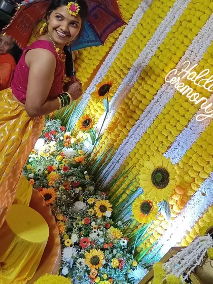 A beautiful shot of the bride posing with a small umbrella against the sunflower-themed Haldi backdrop.