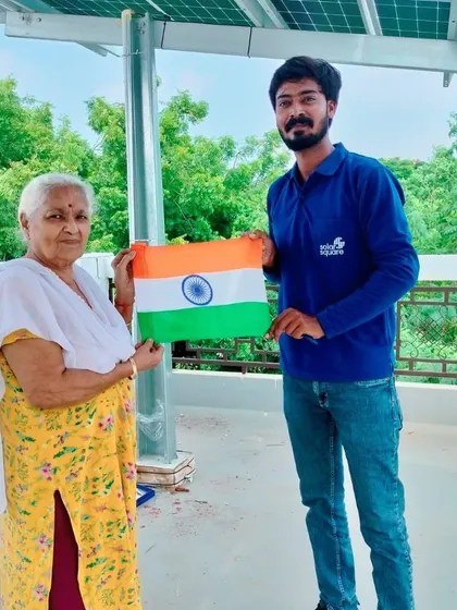 An elderly woman holds the Indian flag with our team member, celebrating the move to clean energy for her home.