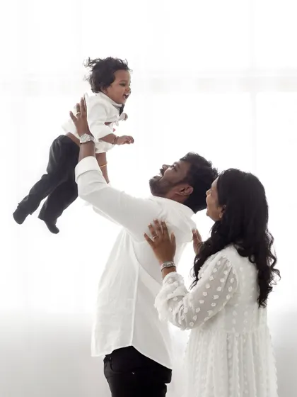A dynamic shot of a father lifting his son in the air while the mother looks on with a smile.