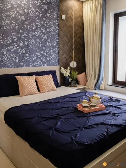 A full view of the bed, showcasing the rich navy blue bedding and the contrasting textures of the wallpaper and wood paneling.