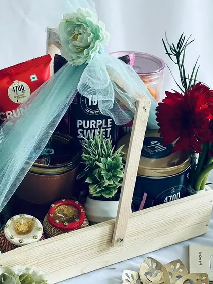 The hamper includes a table planter, traditional diyas, a coffee tumbler, and a selection of gourmet popcorn and snacks.