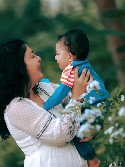 A mother shares a happy, playful moment with her baby boy. The natural green background and soft lighting are perfect for creating warm and authentic family photos.