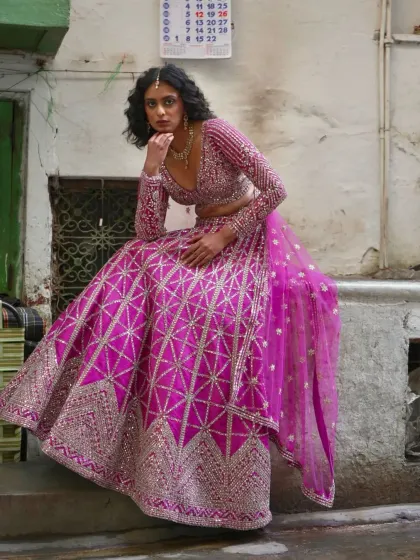 A pensive shot of the model in the pink geometric lehenga, highlighting its unique design and bold color.
