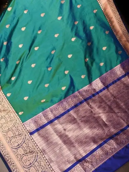 A beautiful teal green silk saree with a contrasting blue and silver border. The small butis on the body add a delicate shimmer to this elegant piece.