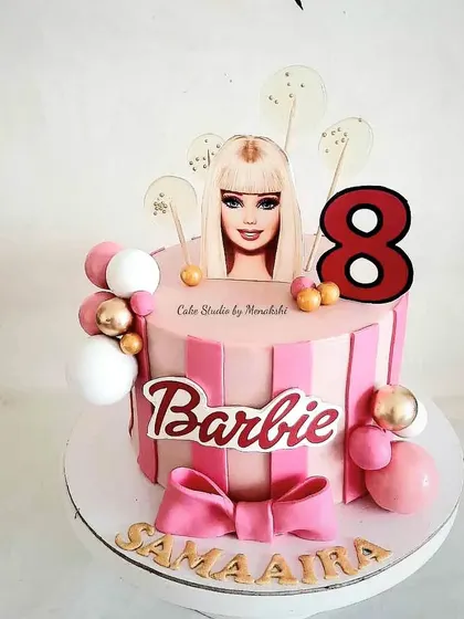 A Barbie themed cake for an 8th birthday. This pink striped cake is decorated with a large bow, spheres, and a Barbie topper for a fun and stylish look.
