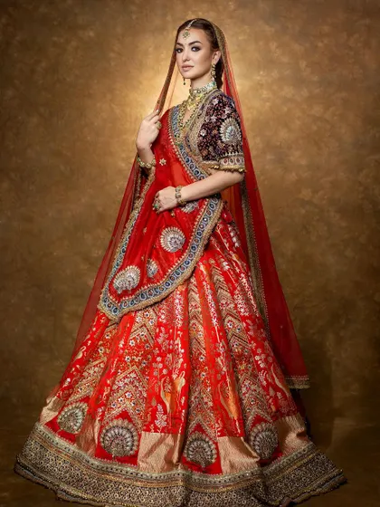 A majestic bridal look featuring a rich red lehenga with a contrasting velvet blouse. This shot captures the full splendor and heritage feel of the design.