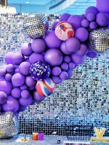 A shimmering silver sequin wall decorated with a purple balloon garland and disco balls. This made for a glamorous photo backdrop at the Rockstar party.