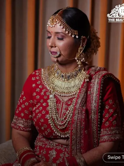 A serene moment captured before the ceremony. This classic bridal makeup features soft, shimmering eyes and a bold red lip, perfectly matching her traditional red lehenga and heavy gold jewellery.