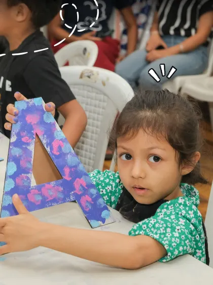 A young girl holds up a large letter 'A' that she has painted with a beautiful, multi-colored design during a creative birthday party.
