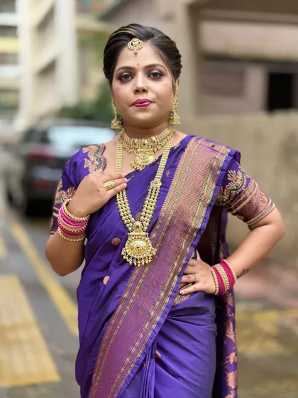A full portrait from a makeup demonstration, showing how to style a client with a purple saree, heavy gold jewellery, and a confident pose.