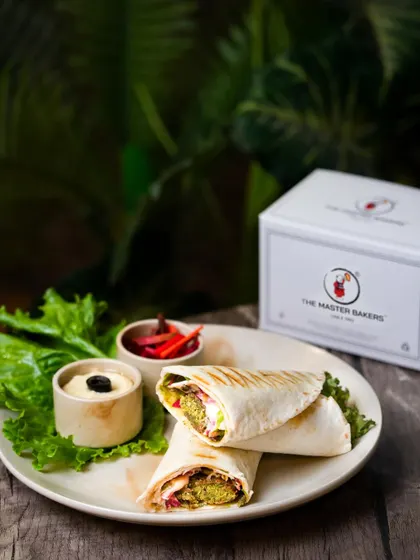 Our finished Falafel Wrap, cut in half to reveal the delicious fillings inside. It's served with hummus and pickled vegetables on the side.