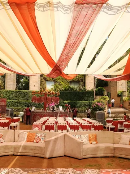 A wide view of the Souk Bazaar Mehndi setup, showing the flowing orange and cream drapes creating a tent-like ceiling over the entire event space, transporting guests to a desert oasis.