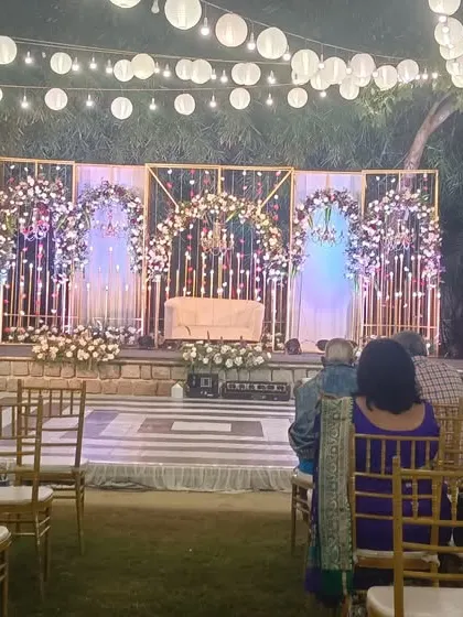 An elegant outdoor reception stage with a backdrop of shimmering lights and floral arches, creating a magical ambiance.