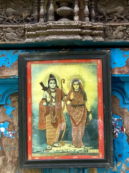 A cloth oleograph of Rama and Sita, set against a vintage architectural piece. The artwork is a multi-color print on cloth, enhanced with hand-done embroidery to add depth and character.