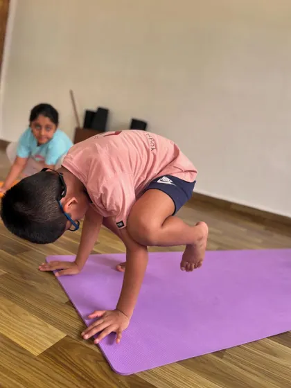 A young student bravely attempts Bakasana, or Crow Pose. Even the effort of trying builds immense strength and confidence.
