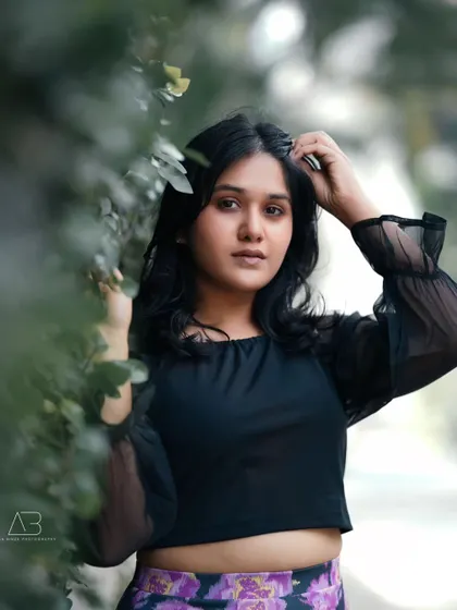 An outdoor portrait using natural elements to frame the subject. Her direct gaze and the soft, diffused light create a beautiful and engaging fashion-style shot.