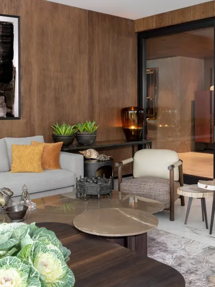 A living room corner where every object is chosen to speak without speaking. The grain of the custom veneer, the texture of the cushions, and the collected shells and sculptures all contribute to a layered, warm, and soulful environment.