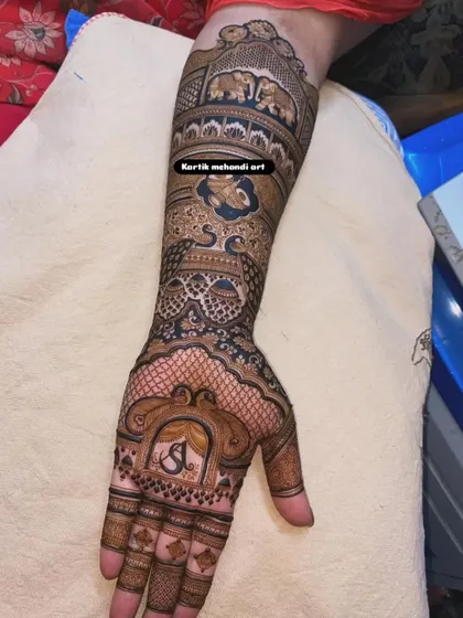 A close-up of a traditional design featuring the couple's initial 'S' in a beautiful frame. The arm is adorned with elephant motifs and intricate patterns.