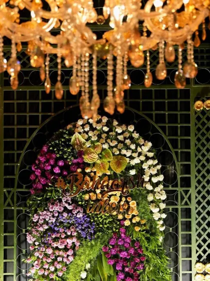 A floral crest with the couple's initials adds a personalized touch to the decor. This element was placed under a chandelier against a green lattice wall, making it a beautiful focal point.